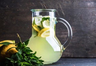 Homemade lemonade with mint, lemon slices and ice over dark background, copy space